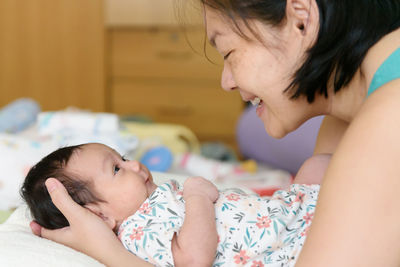 Asian mom hands around a young daughter lying in bed smile and look at each other