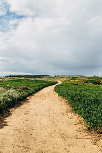 Dirt road amidst field against sky