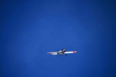Low angle view of airplane flying against clear blue sky