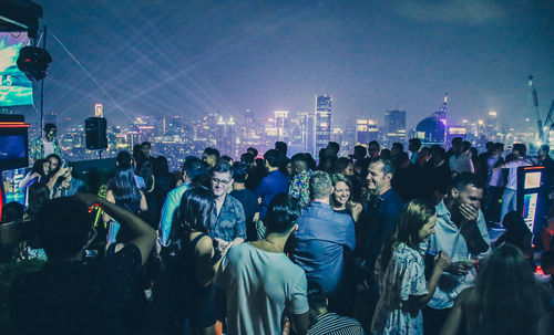 Crowd at music concert in city against sky at night