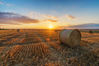 Hay bales on field against sky during sunset