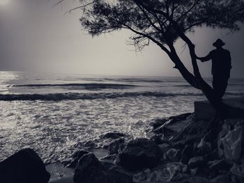 Man standing on rock at beach against sky