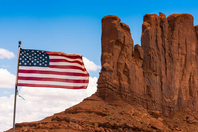 Low angle view of flag waving by rock formation against sky