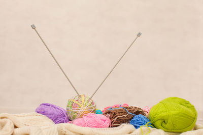 Colorful wool balls with knitting needles against wall