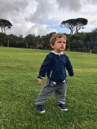 Full length of boy looking away while standing on field against cloudy sky