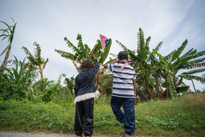 Rear view of siblings holding malaysian flags on field