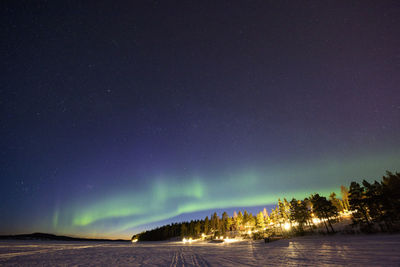 Aurora polaris over landscape against sky at night during winter