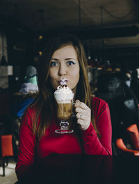 Portrait of woman holding drink while sitting in restaurant