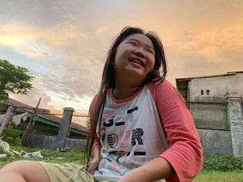 Portrait of smiling woman sitting against sky during sunset