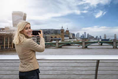 Portrait of young woman photographing with mobile phone in city