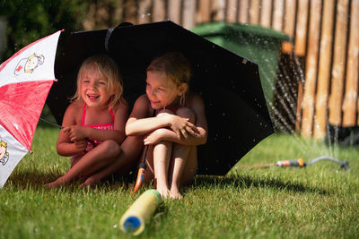 Sisters with umbrellas sitting on grassy field at backyard