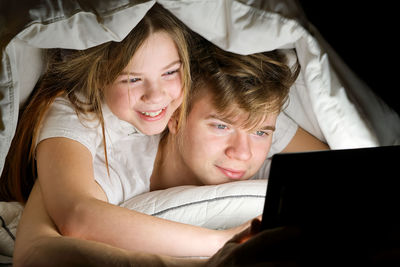 Brother and sister using digital tablet under blanket