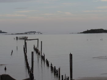 Wooden posts in sea against sky at sunset