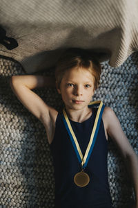 Directly above portrait of boy wearing medal and lying on carpet at home