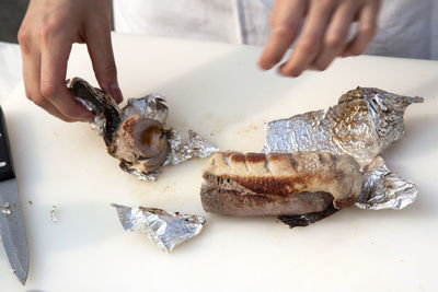 Cropped hands of chef removing sausage from foil on table