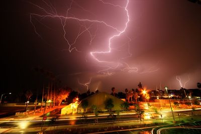 Lightning over illuminated city against sky at night