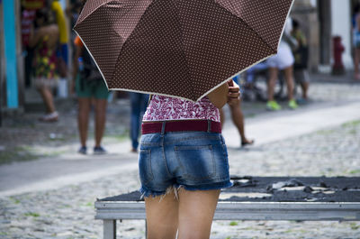 A woman from the back holding a brown umbrella on the street. salvador, bahia, bahia.