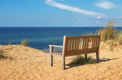 Empty chairs on beach by sea against sky