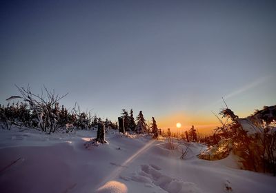 Snow covered field against sky during sunset