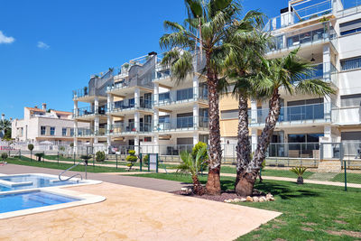 Palm trees by swimming pool by building against sky