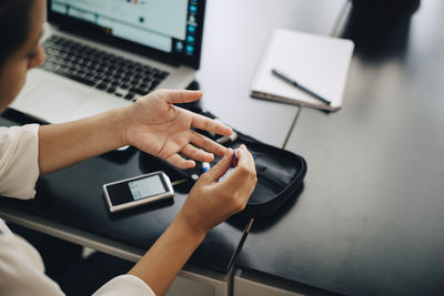 Cropped businesswoman doing blood test by laptop at desk in office