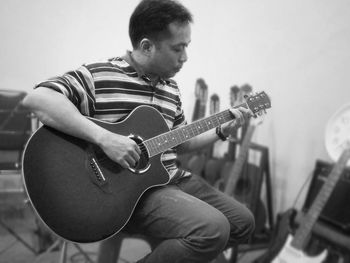 Mature man playing guitar while sitting on chair against wall