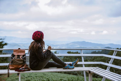 Woman sitting on bench on mountain and sky