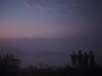 People standing on land against sky during sunset