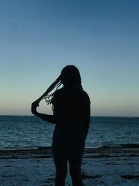 Rear view of silhouette woman standing at beach against clear sky