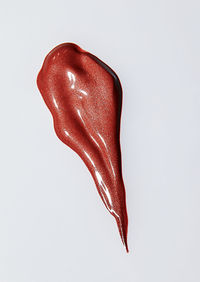 High angle cosmetic smear of iridescent creamy red makeup on white background