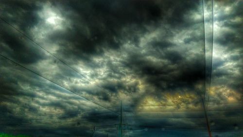 Low angle view of power lines against cloudy sky