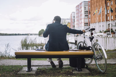 Rear view of businessman talking on smart phone while sitting near bay