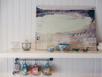 Cups hanging by picture frame on shelf