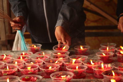 Midsection of man holding burning candles in temple