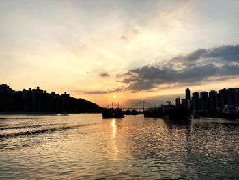 Silhouette buildings by river against sky during sunset