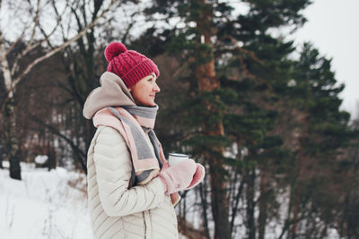 Side view of woman wearing warm clothing against tree