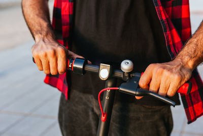 Unrecognizable crop male in checkered shirt riding modern electric scooter along pavement in city