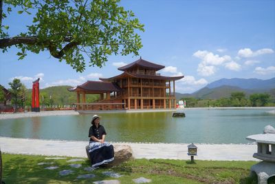 Woman sitting by lake against sky