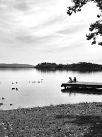 View of people in calm lake against cloudy sky