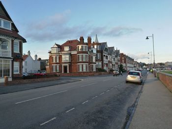 Cars on road by buildings in city against sky