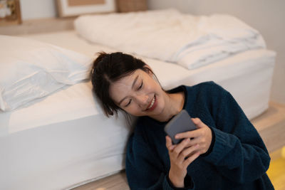Young woman using mobile phone while lying on bed at home