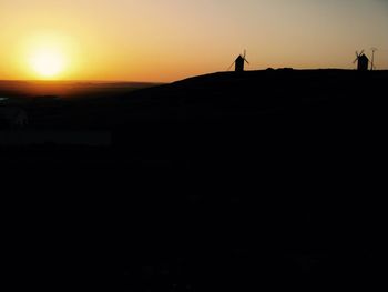 Low angle view of silhouette traditional windmills on mountain against clear sky during sunset