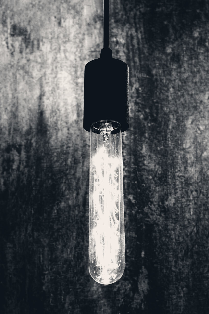 CLOSE-UP OF ILLUMINATED LIGHT BULB AGAINST WALL