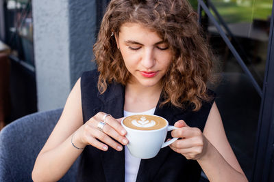 Young beautiful happy woman with curly hair enjoying cappuccino in street cafe, summer time