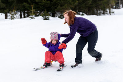 Full length of mother with daughter skiing on snow