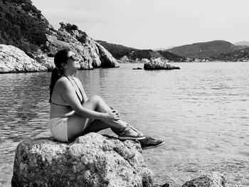 Young woman sitting on rock by sea