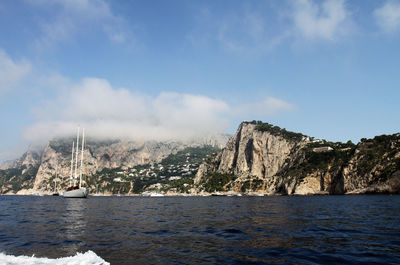 Scenic view of sea by mountain against sky