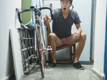 Surprised young man pointing at his bicycle indoors 