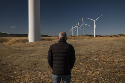 Adult man in winter cloth with modern windmills against blue sky. shot in castilla la mancha, spain