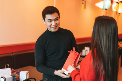 Beautiful young asian couple in red clothes give present in festive chinese vietnamese restaurant 